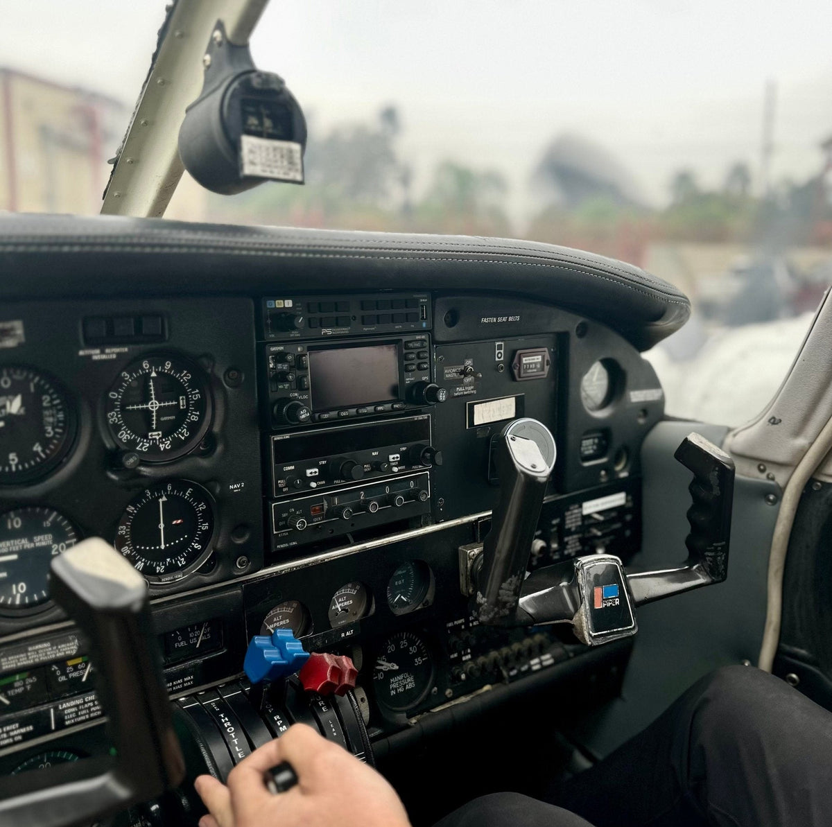 Hand on the throttle below the instrument panel of a Piper trainer, ready to fly