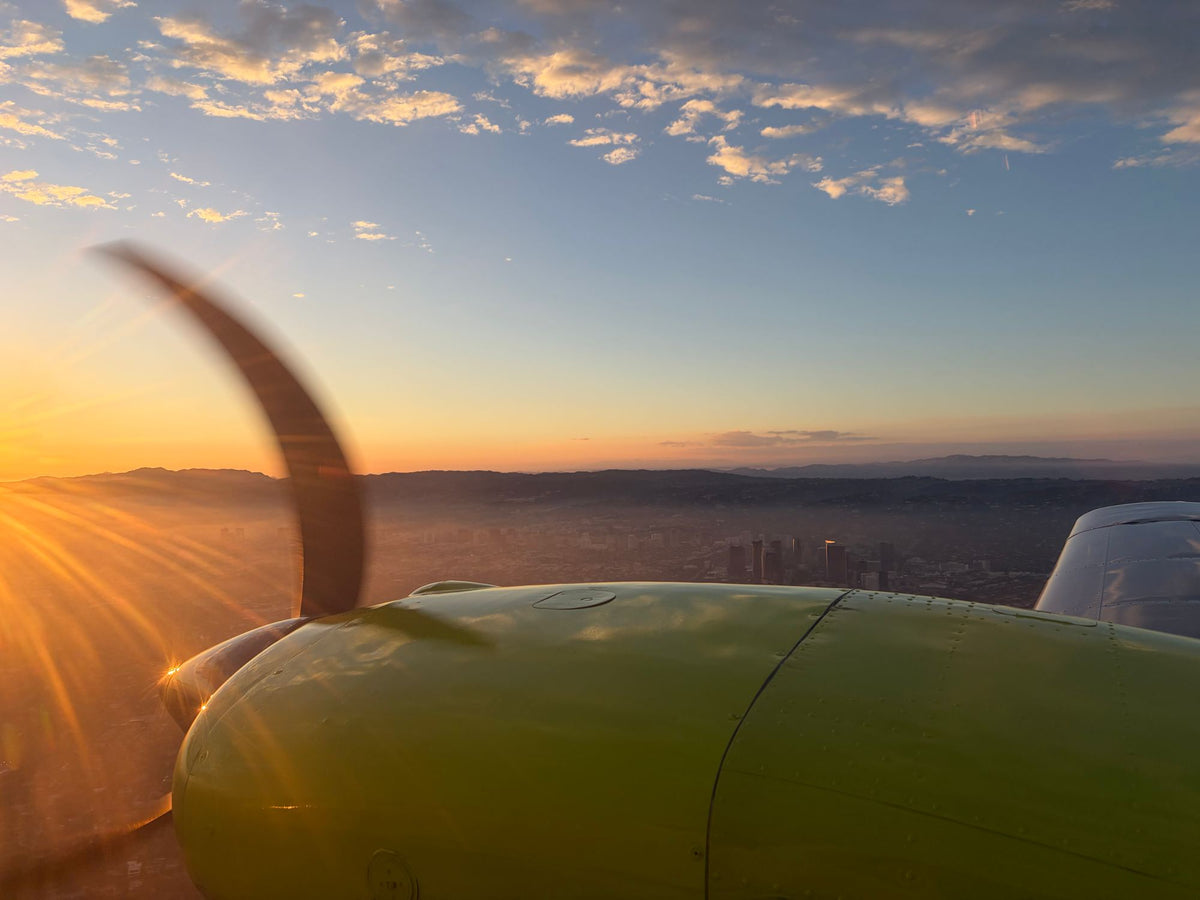 Piper Seminole engine nacelle and propeller in flight at sunset with the Los Angeles skyline and hills on the horizon