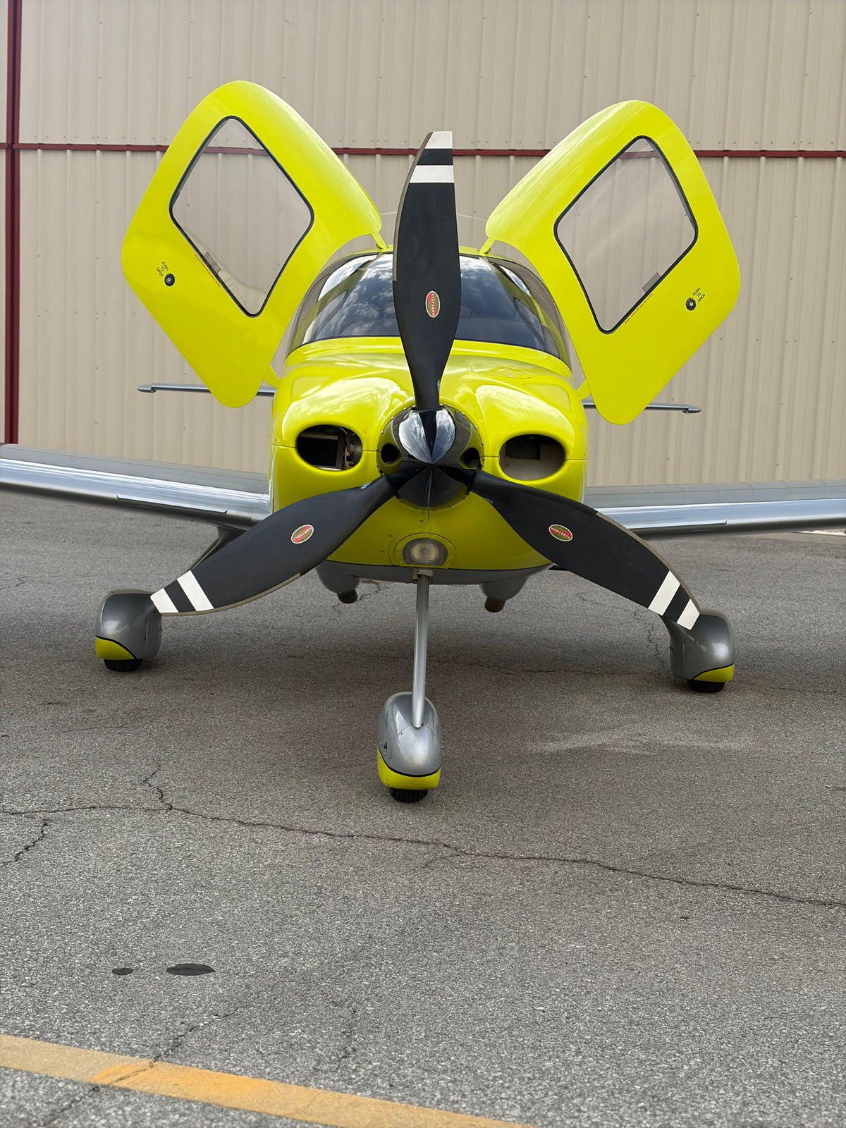 Yellow Cirrus SR22 facing the camera with both doors open on the ramp, portrait view