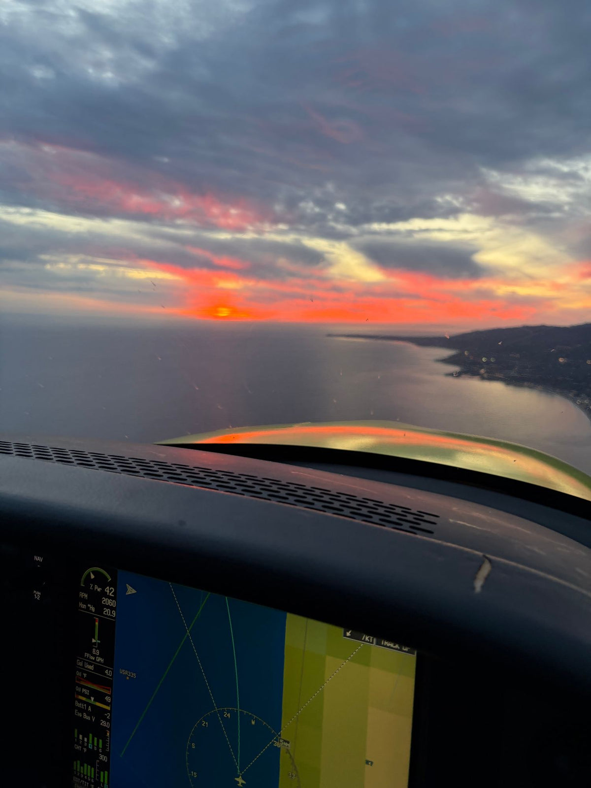 Moving-map display on the instrument panel with the coastline and a red sunset beyond the windshield