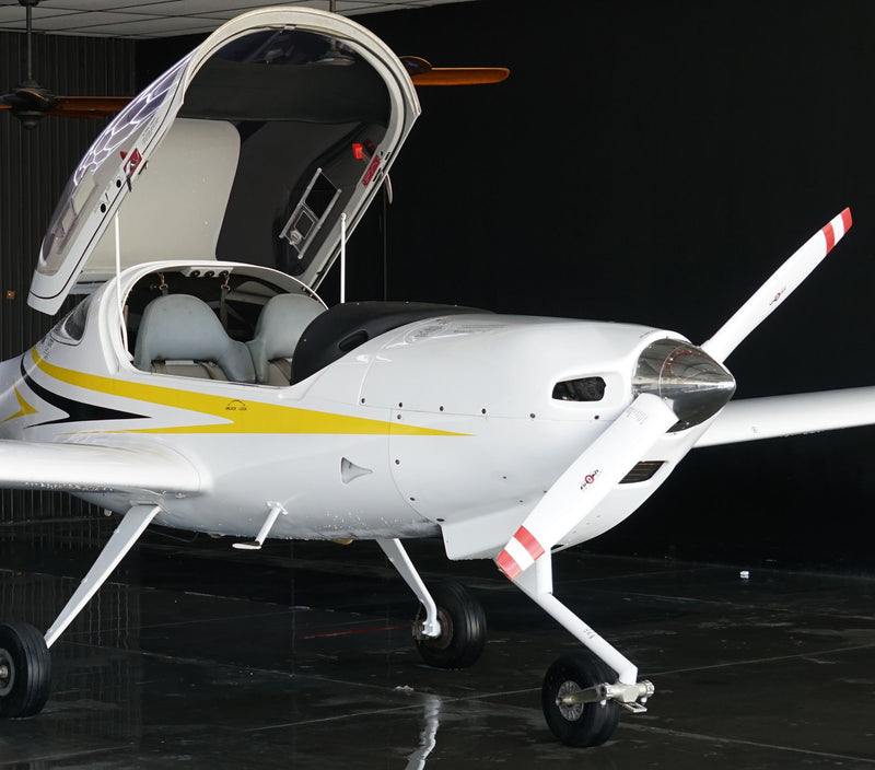 A white Diamond DA20-C1 trainer with its bubble canopy raised in a hangar at Van Nuys