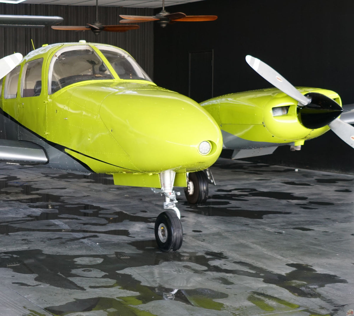 Yellow Piper Seminole nose and right engine inside a dark hangar with a wet, reflective floor