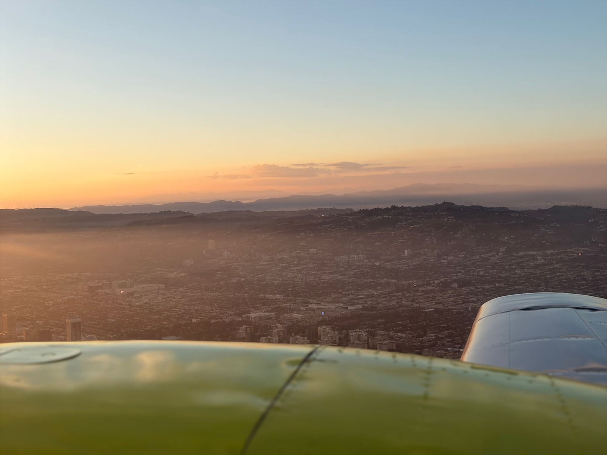 Hazy sunset over the hills of Los Angeles seen over a yellow engine nacelle, with the second engine visible at right