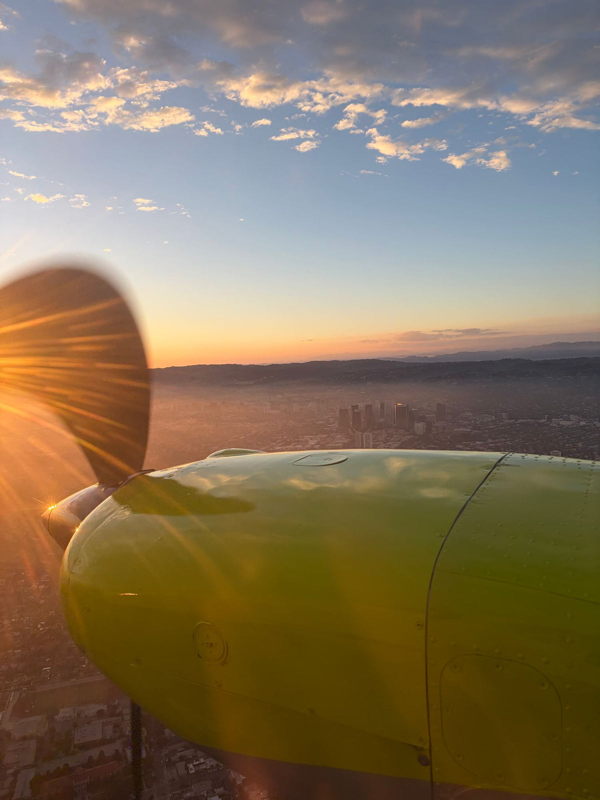 Yellow engine nacelle and turning propeller of a Piper Seminole in flight with the sun low over Los Angeles