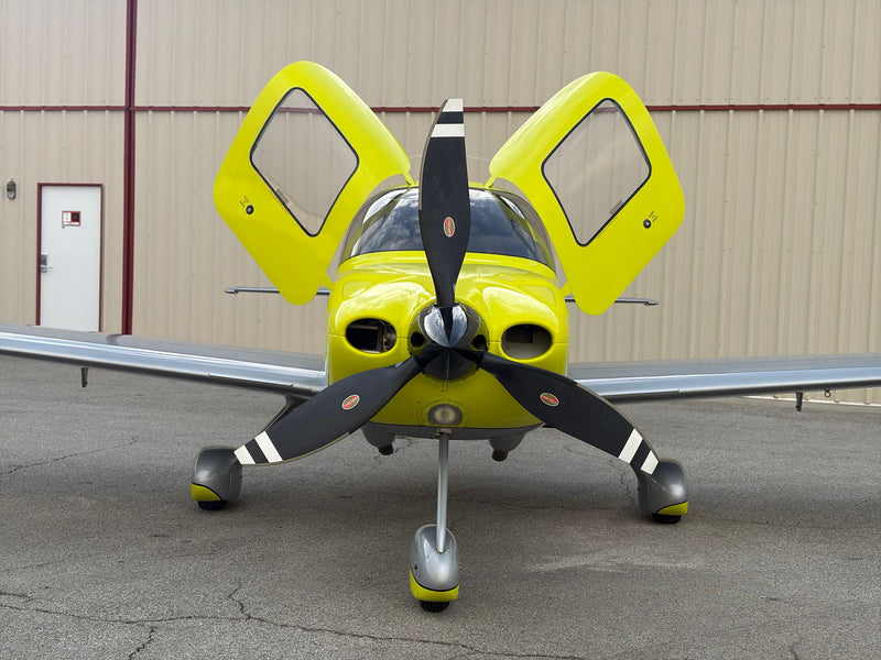 A yellow Cirrus SR22 Turbo head-on with both doors raised in front of a hangar at Van Nuys