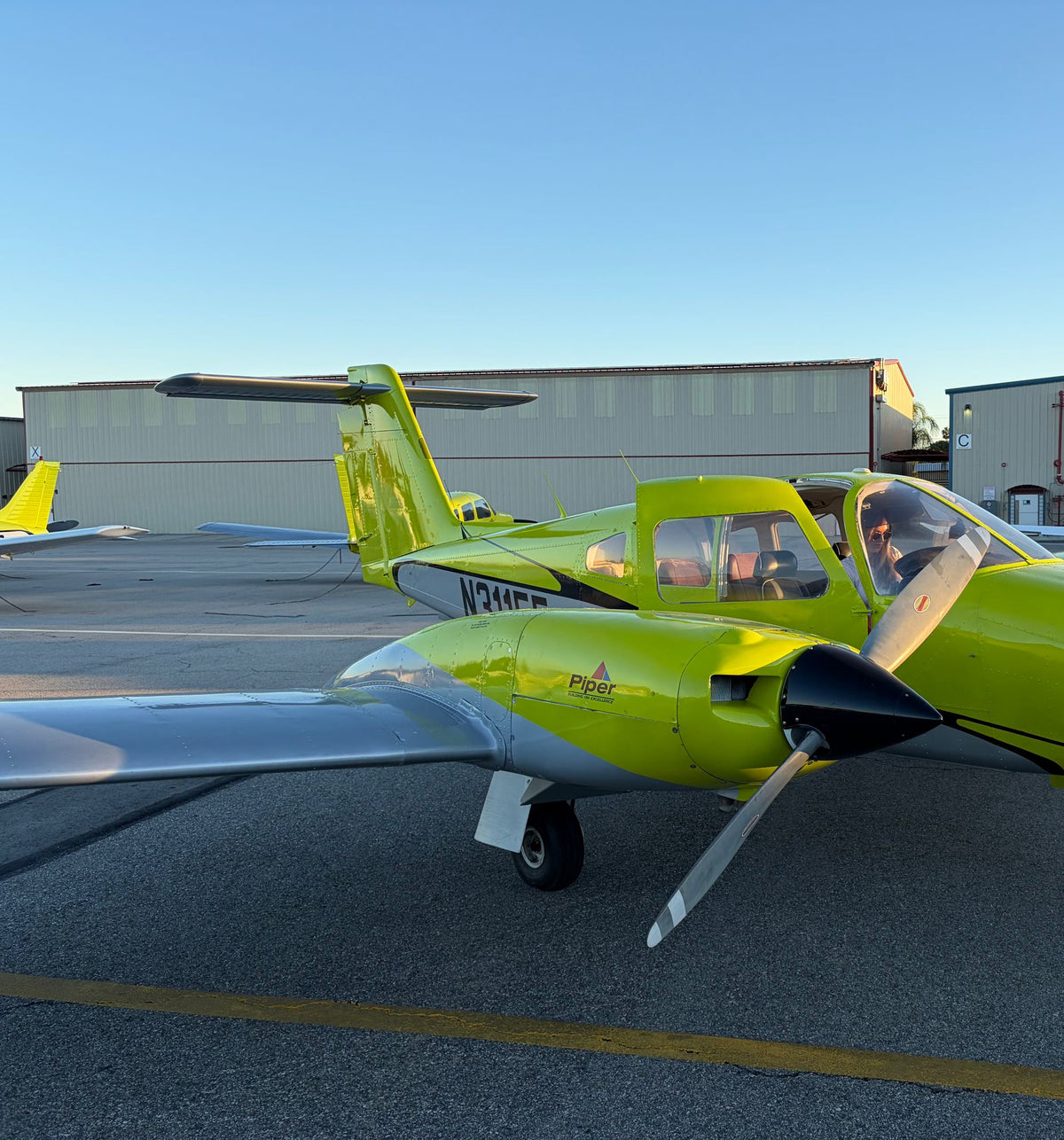 Yellow Piper Seminole N311EF on the ramp in late-day sun with people seated in the cockpit