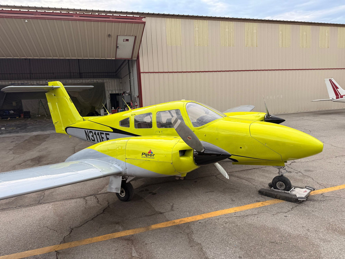 Yellow twin-engine Piper Seminole N311EF parked on the ramp in front of an open hangar