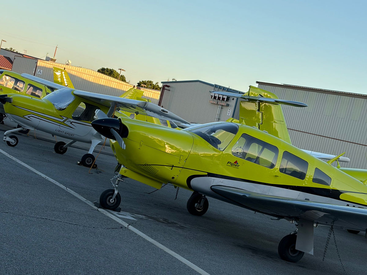 Low-angle view of a yellow Piper trainer with Cessna 162s and a twin parked behind it near the hangars