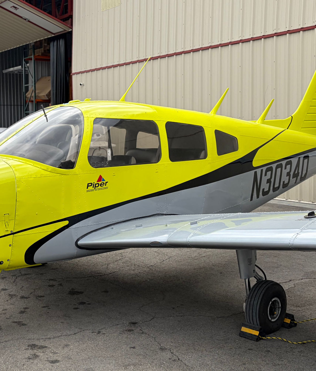 Close side view of the cabin windows, wing and N3034Q registration on a yellow Piper Warrior