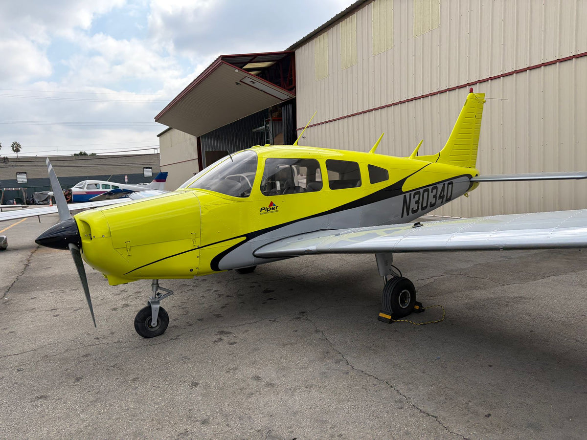 Yellow Piper Warrior N3034Q parked beside a tan hangar at Van Nuys Airport
