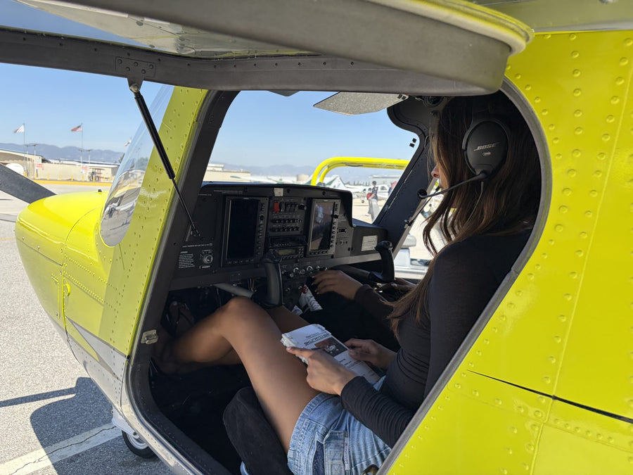 Student pilot with the door open reading a checklist on her lap in a Cessna 162